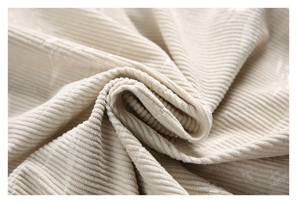 Close-up of cream corduroy fabric loosely folded to show its raised ribbed texture.