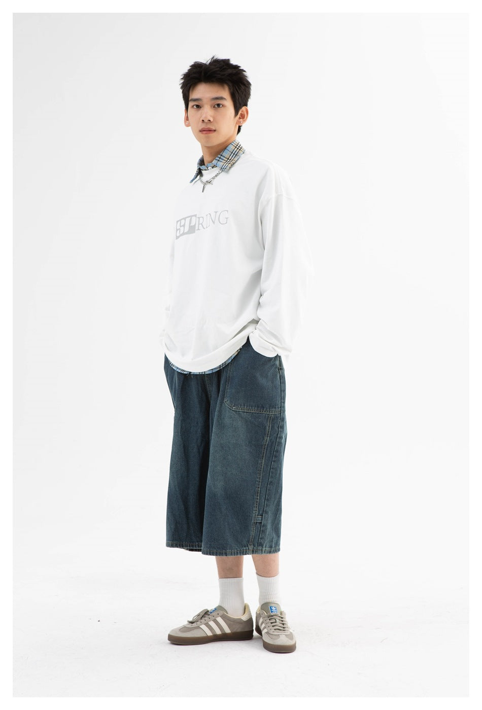 Model wearing the white long-sleeve top with chest SPRING graphic over a plaid collar, with denim shorts and sneakers
