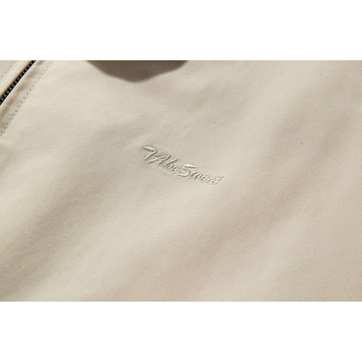 Close-up of beige jacket fabric with an embroidered Timberland logo.