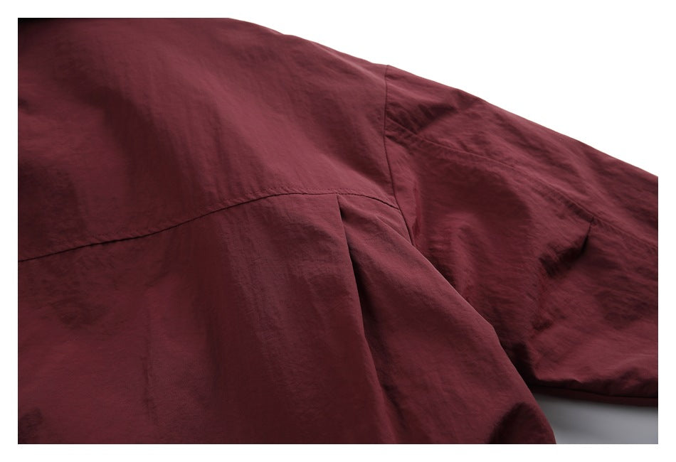Close-up of a burgundy jacket's back yoke seam, sleeve, and gathered fabric.