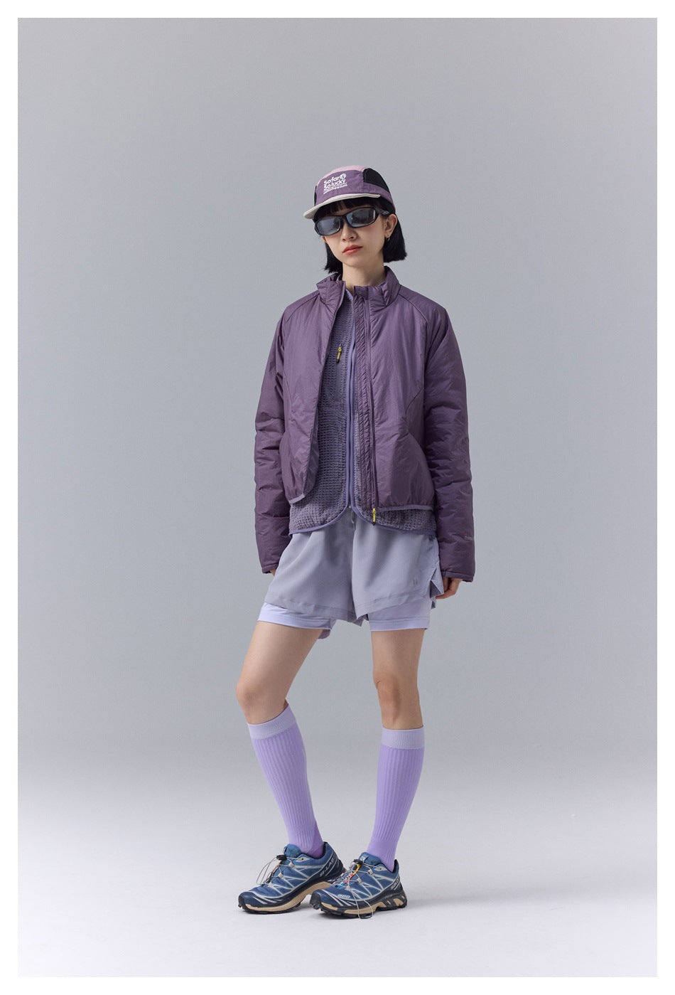 Full-length view of a woman in a purple padded stand-collar jacket with shorts, knee socks and sneakers