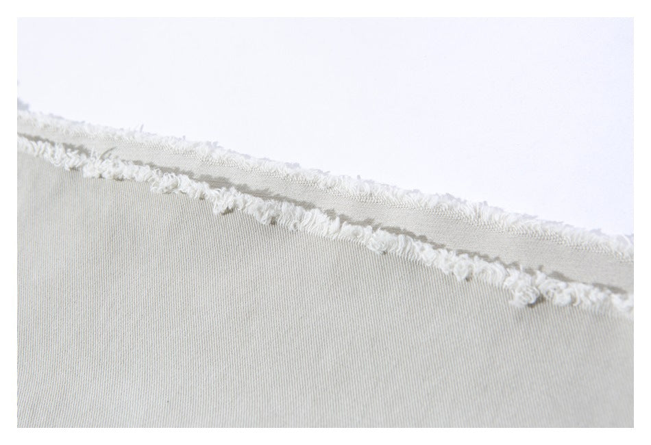 Close-up of light beige trouser fabric with a raw, frayed edge.
