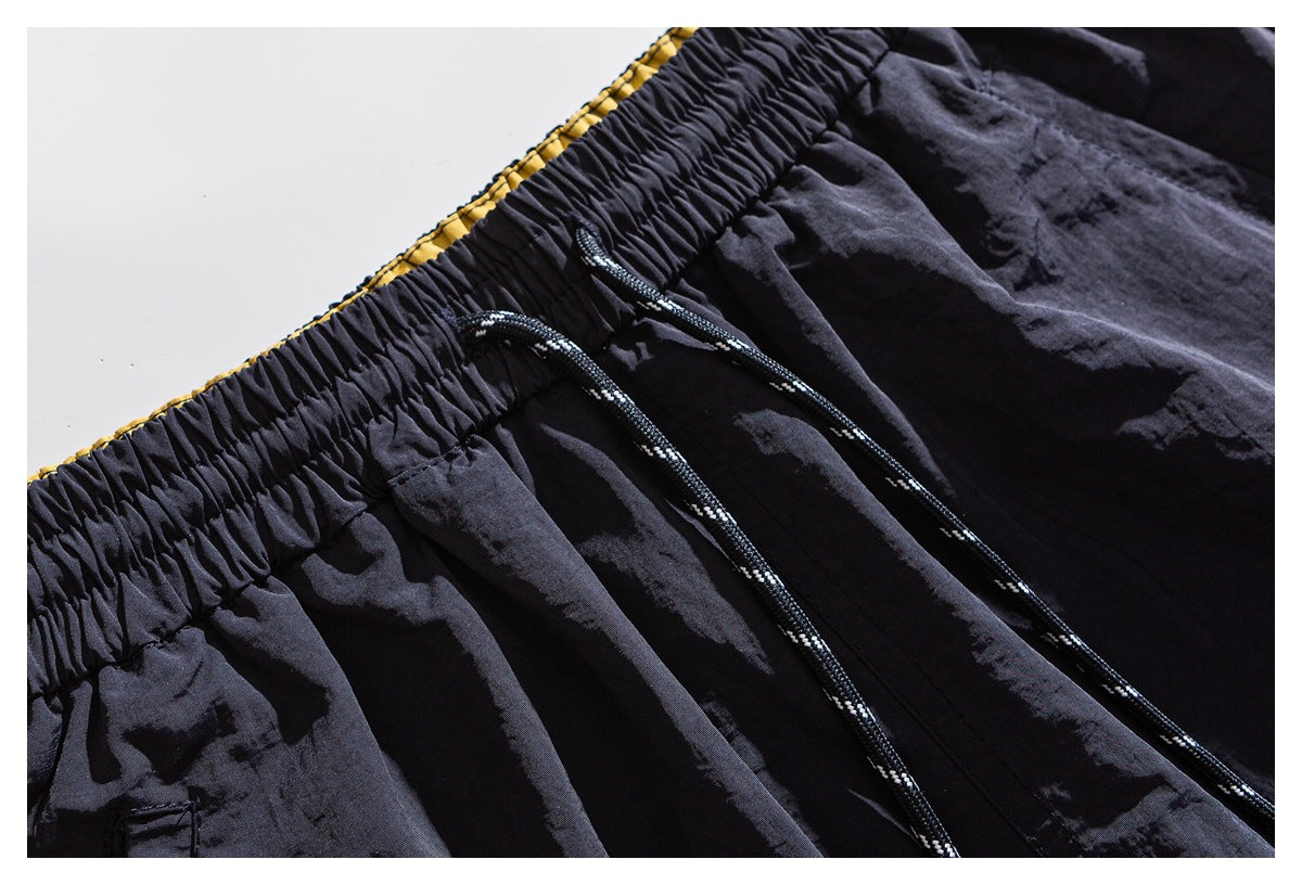 Close-up of dark shorts with a gathered elastic waistband, black-and-white drawstrings, and a narrow yellow lining edge.