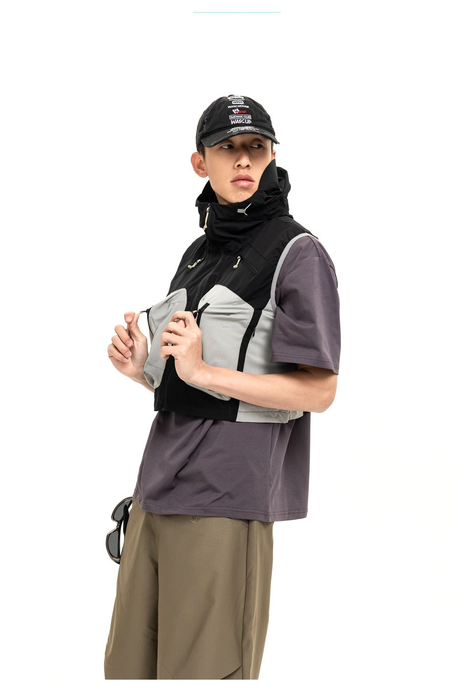 Model wearing a black high-collar vest with pale gray front pockets over a muted purple T-shirt.