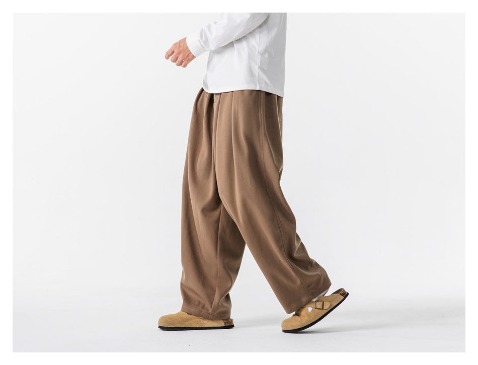 Side view of a person walking in loose taupe-brown trousers and a white long-sleeve shirt.
