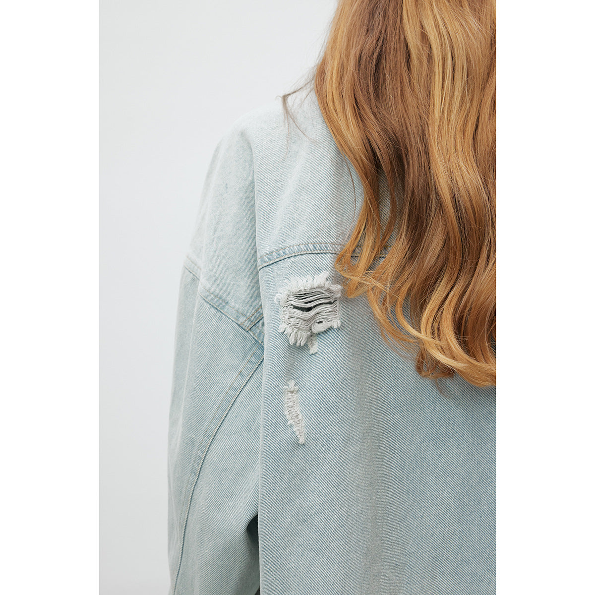Close-up of distressed white-frayed patches on the sleeve and back of a light-wash denim jacket.