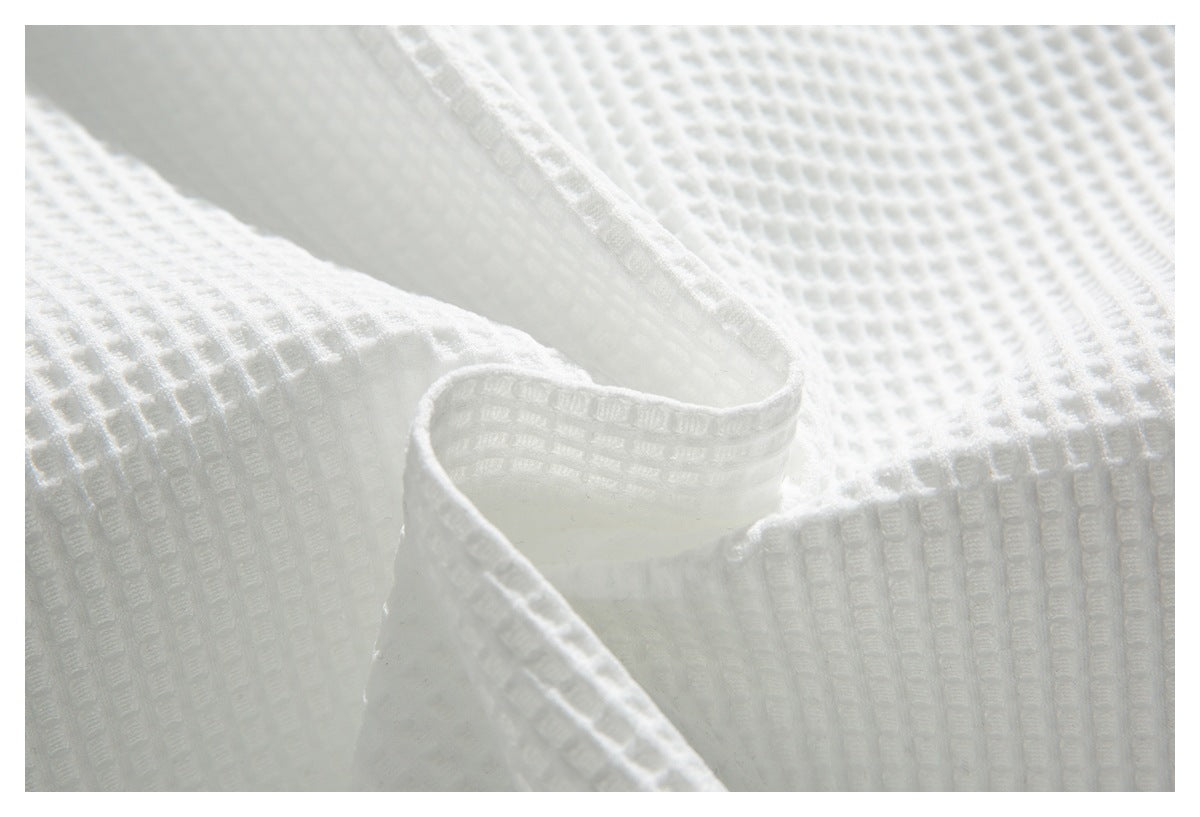 Close-up of white waffle-textured fabric showing a curved folded edge and stitching.