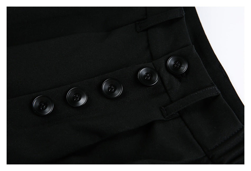 Close-up of black trousers showing four waistband buttons and narrow adjustment tabs.