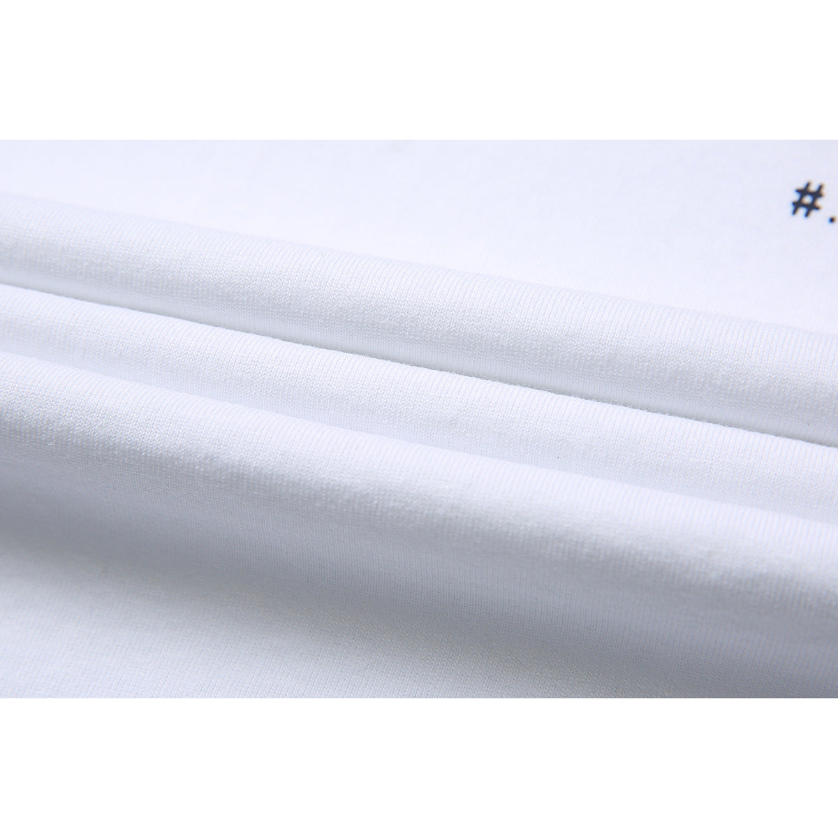 Close-up of folded white T-shirt fabric showing its knit texture and a small cropped dark print.