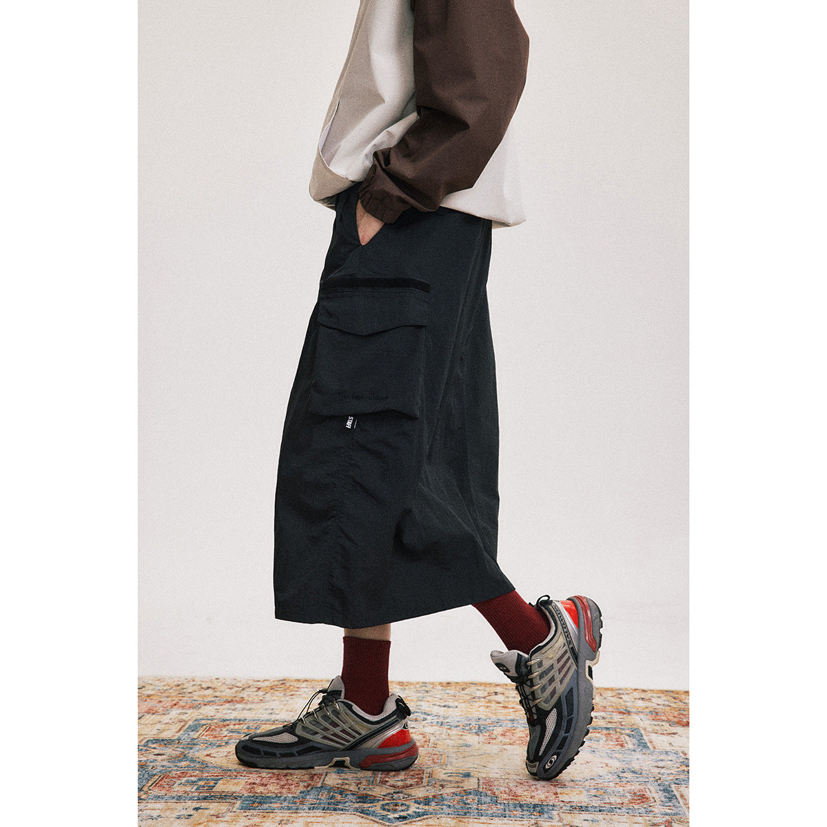 Cropped side view of a model wearing a black mid-calf utility skirt with a large flap cargo pocket.