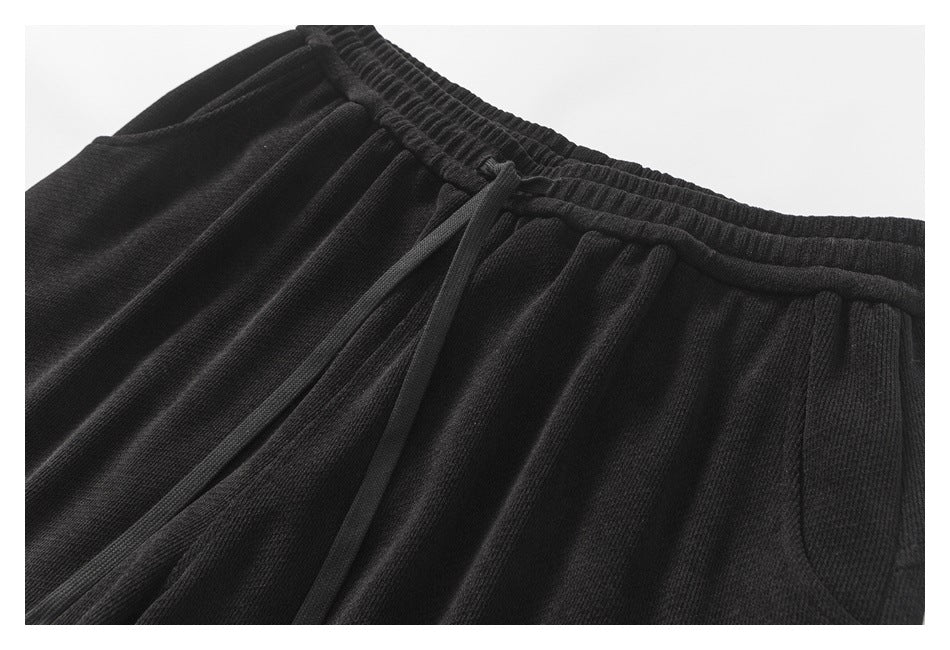 Close-up of black pants showing the gathered elastic waistband, drawstring, and front seam.