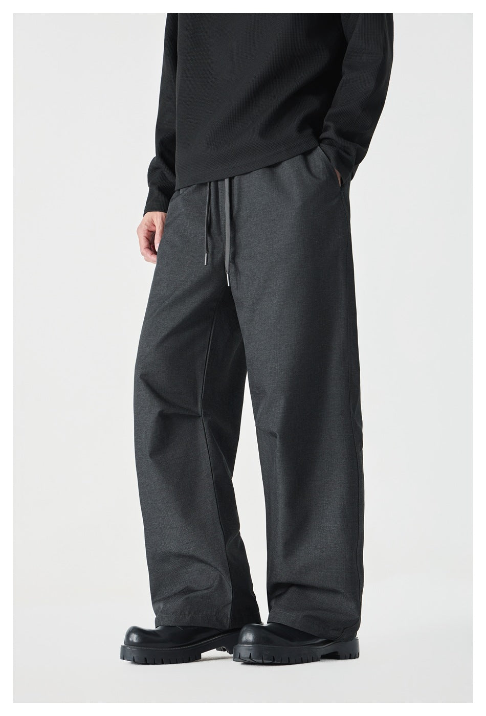 Three-quarter view of a model wearing charcoal wide-leg drawstring pants with side pockets.