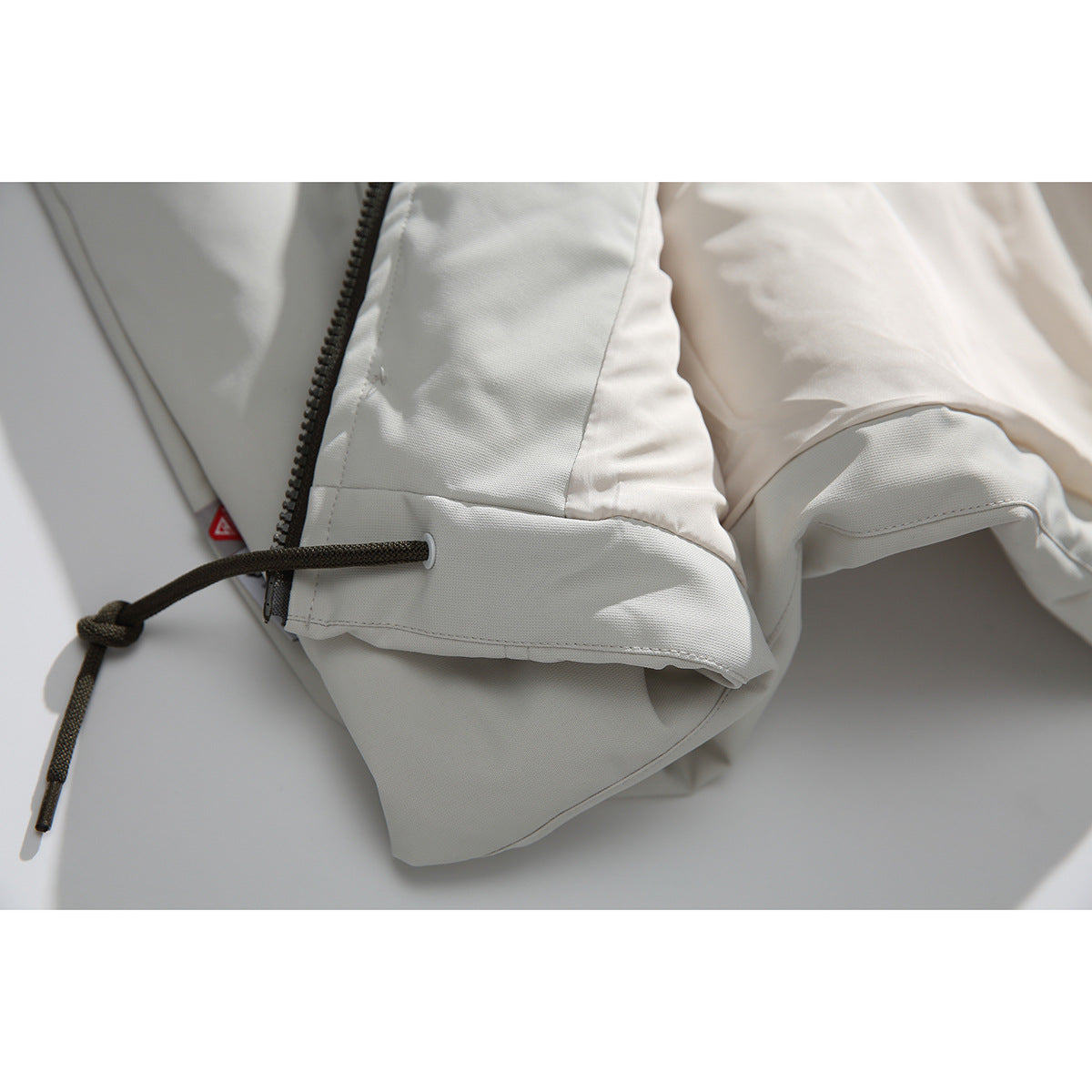 Close-up of an off-white jacket sleeve cuff with a dark drawcord and zipper visible nearby.