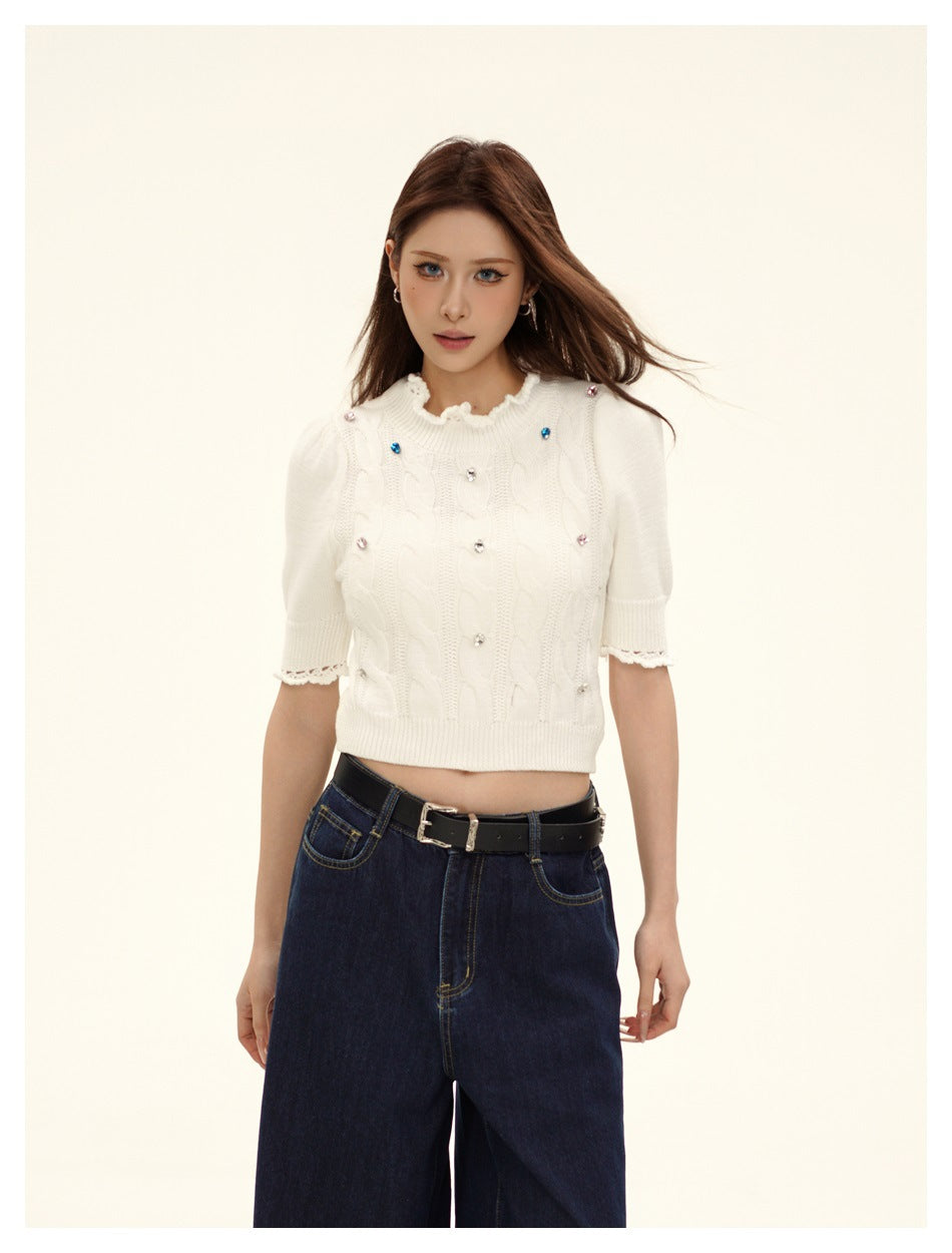 Model wearing a white cropped cable-knit top with jewel embellishments, a ruffled neckline and short puff sleeves.