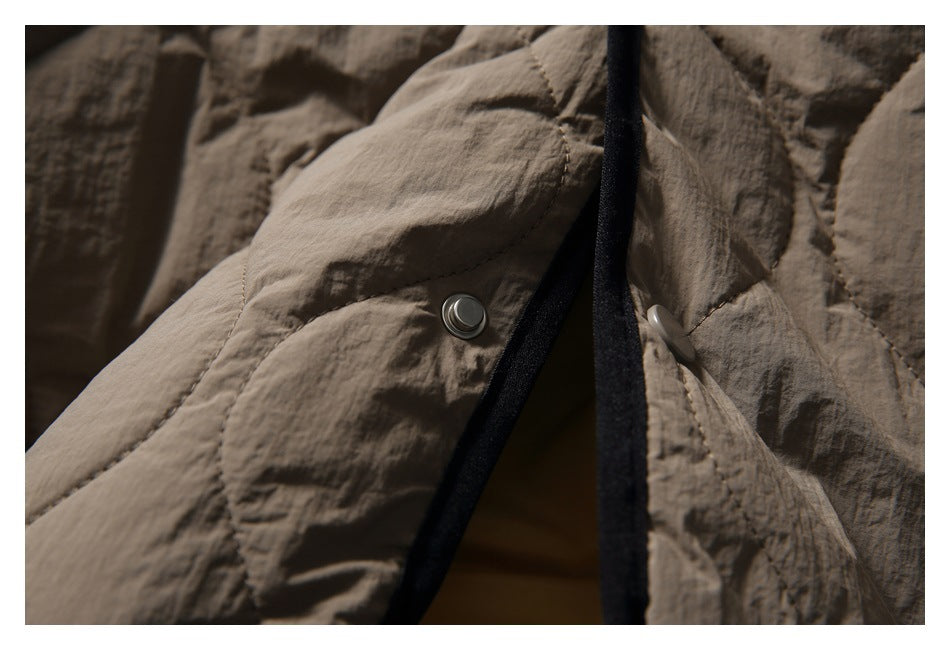 Close-up of a taupe quilted jacket with a metal snap and black edge binding.