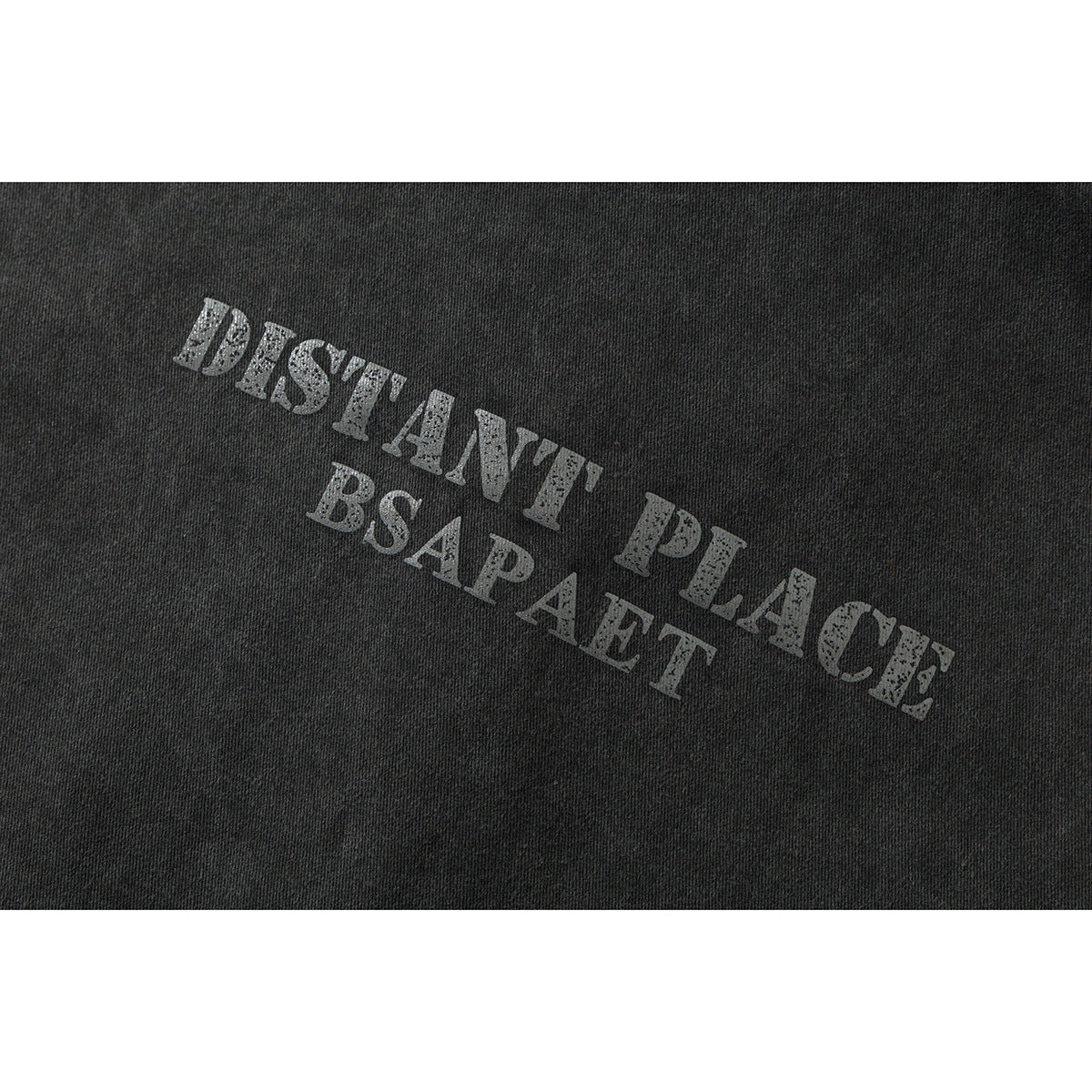 Close-up of distressed gray English lettering printed on charcoal fabric: “DISTANT PLACE BSAPAET.”