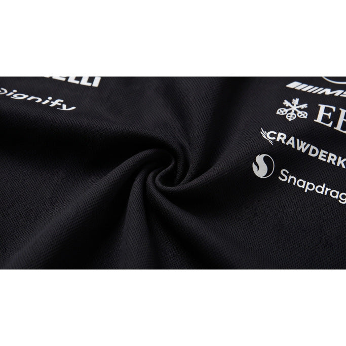 Macro view of black textured polo fabric gathered in a swirl, with white sponsor prints visible at the edge.