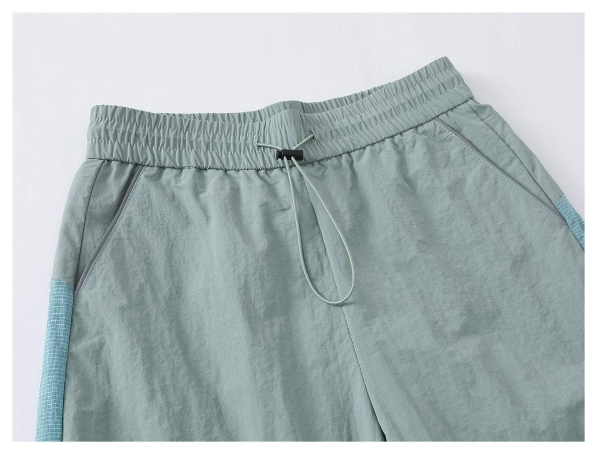 Close-up of pale sage pants' front waistband and drawcord, with slanted pockets and blue grid-patterned side panels.