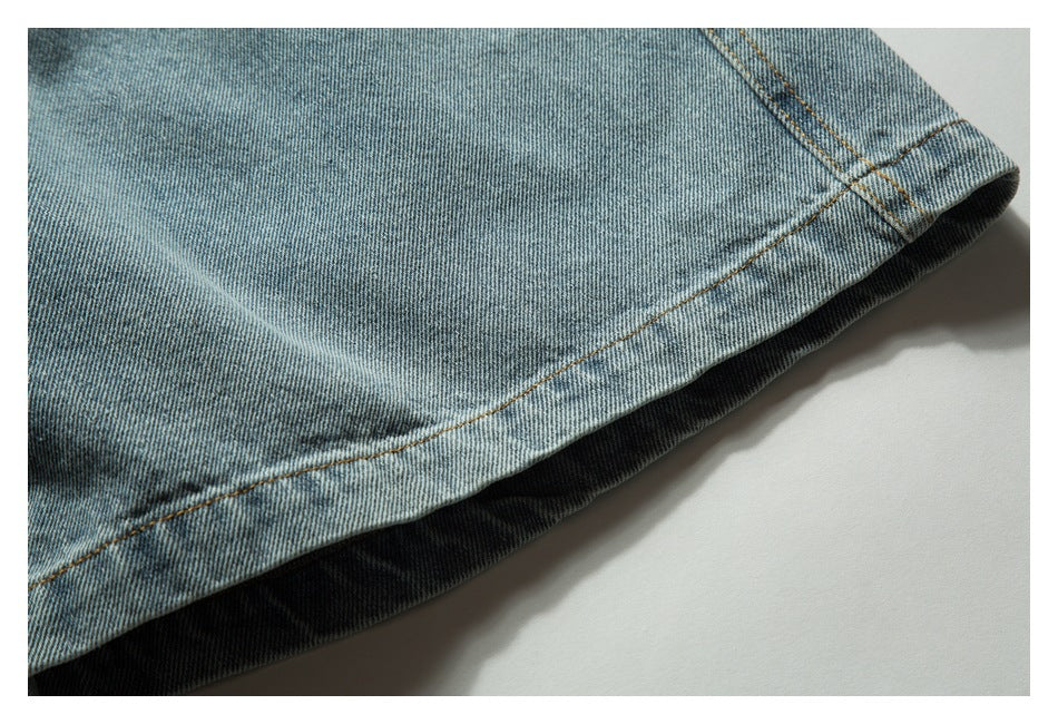 Close-up of the curved hem and tan stitching on light blue denim shorts.