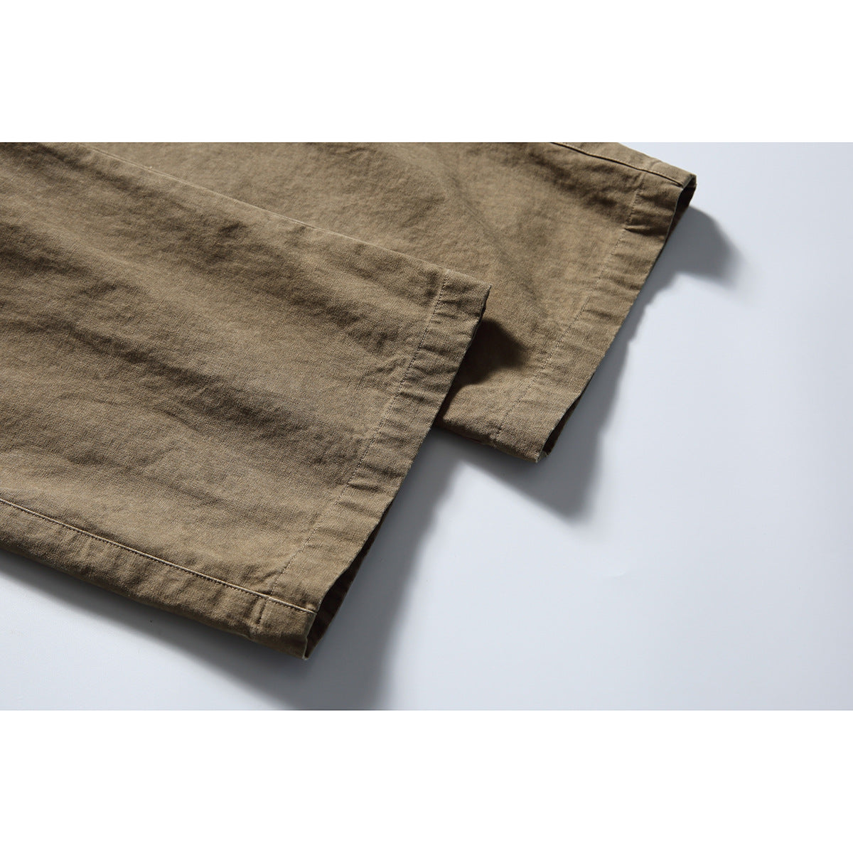 Close-up of the stitched hems of olive-brown pants, with overlapping fabric legs.