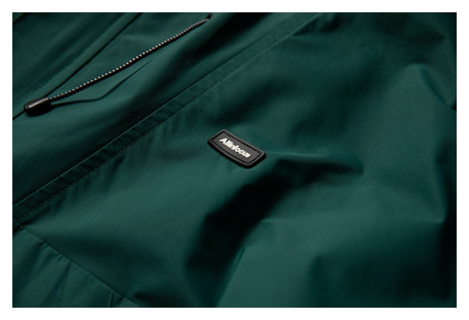 Close-up of a small branded patch on the dark teal jacket beside a stitched seam and drawcord.