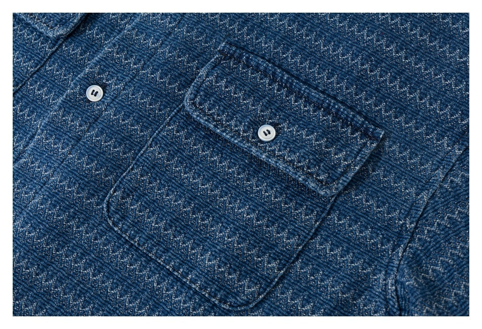 Close-up of a buttoned chest pocket on a blue shirt with a woven zigzag pattern.