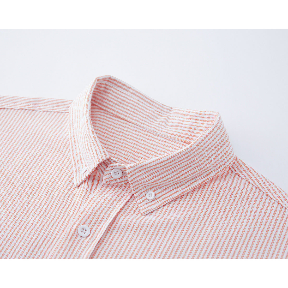 Close-up of a white shirt with fine coral stripes, showing the button-down collar and front buttons.