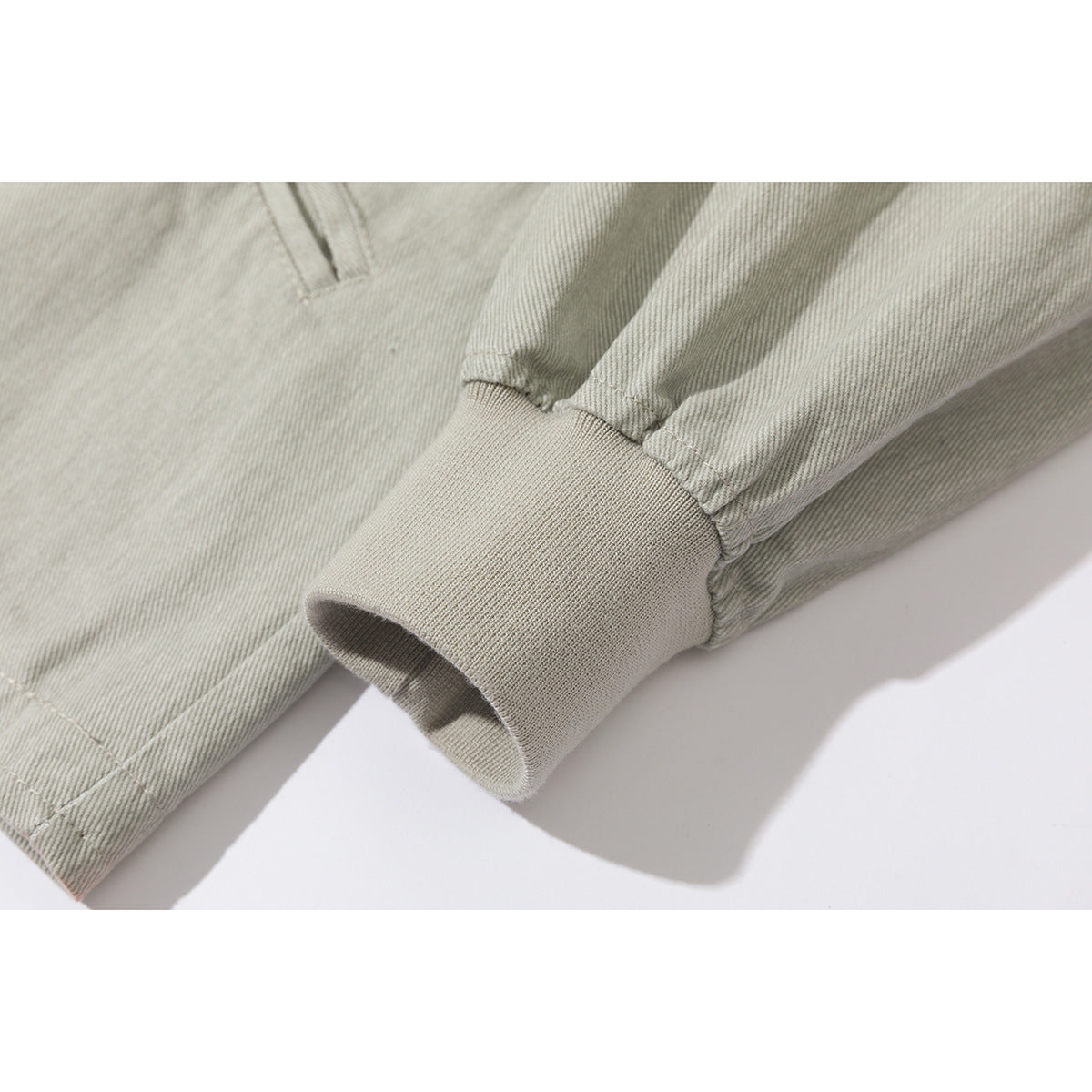 Close-up of a ribbed cuff on the sleeve of a light gray-green jacket.
