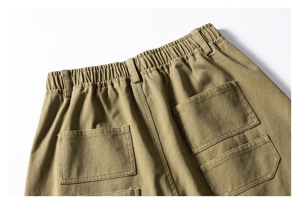Partial back view of khaki trousers laid flat, showing an elastic waistband and patch pockets.