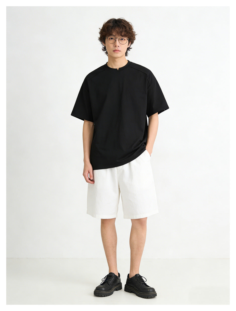 Model wearing a plain black short-sleeve T-shirt with a small center neckline notch and white shorts.