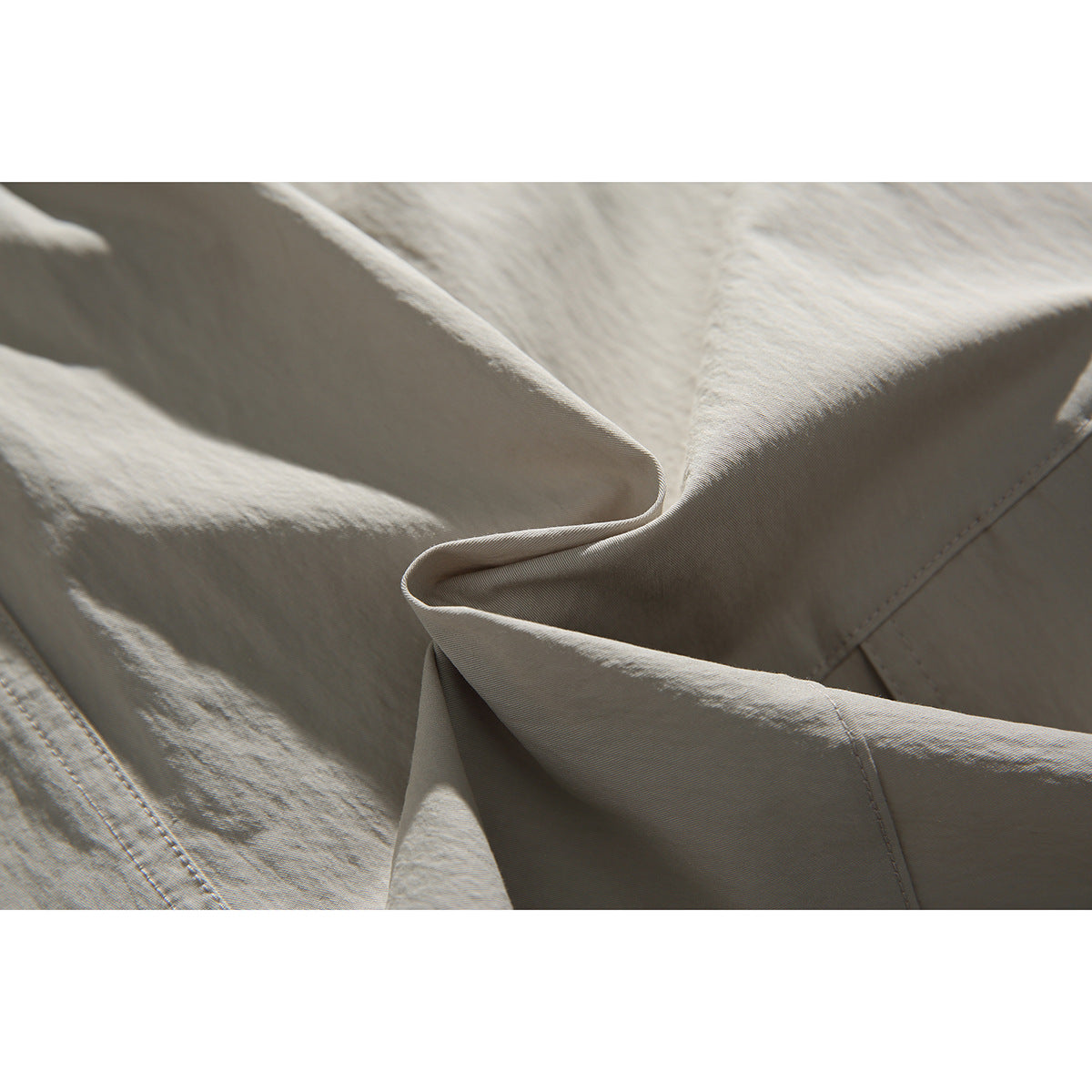 Close-up of light beige shorts fabric folded to show its texture and stitching.