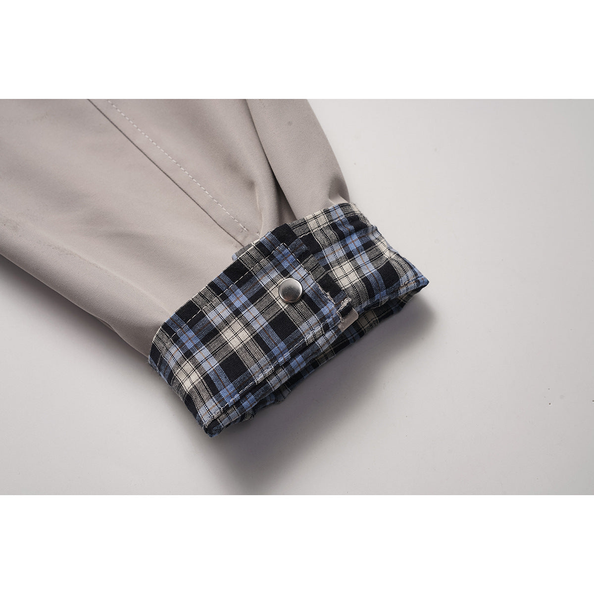 Close-up of a light gray jacket sleeve with a blue, black, and cream plaid cuff and metal snap.