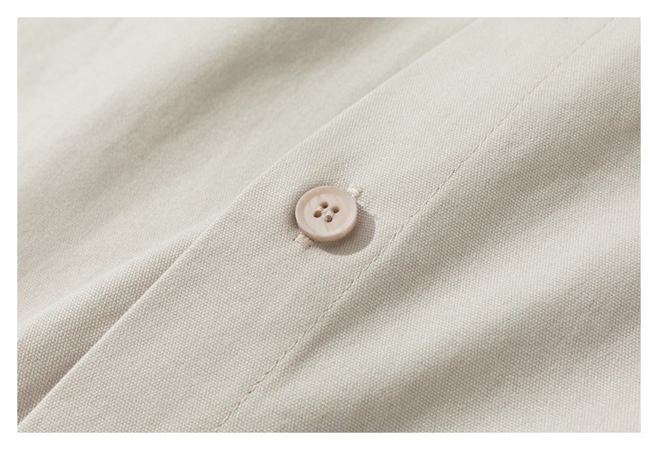 Close-up of cream-colored woven fabric with a matching four-hole button and stitched seam.