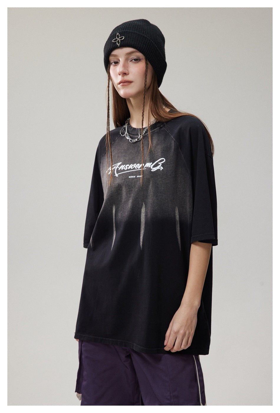 Model wearing an oversized black graphic T-shirt with faded front print and purple cargo pants.