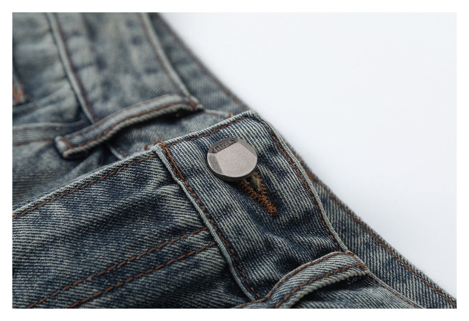 Close-up of a metal button and belt loop on faded blue-gray jeans with brown stitching.
