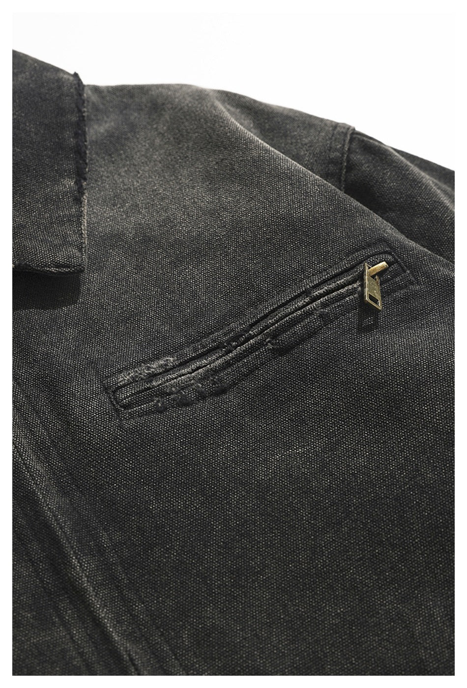 Close-up of a charcoal jacket’s diagonal chest pocket with a brass-toned zipper.