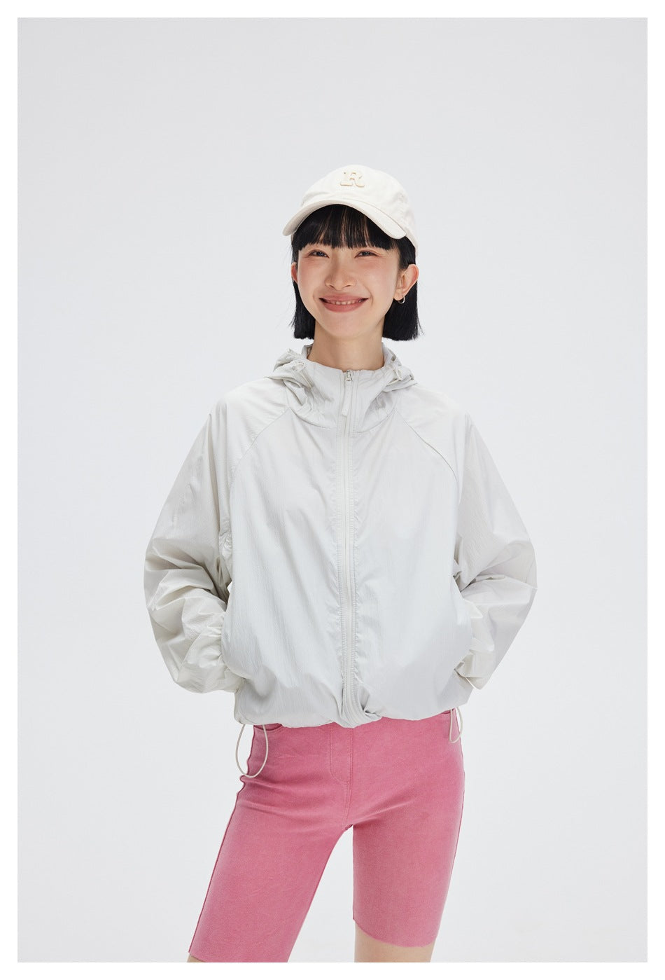 Front view of a model wearing a white hooded zip jacket with pink cycling shorts.
