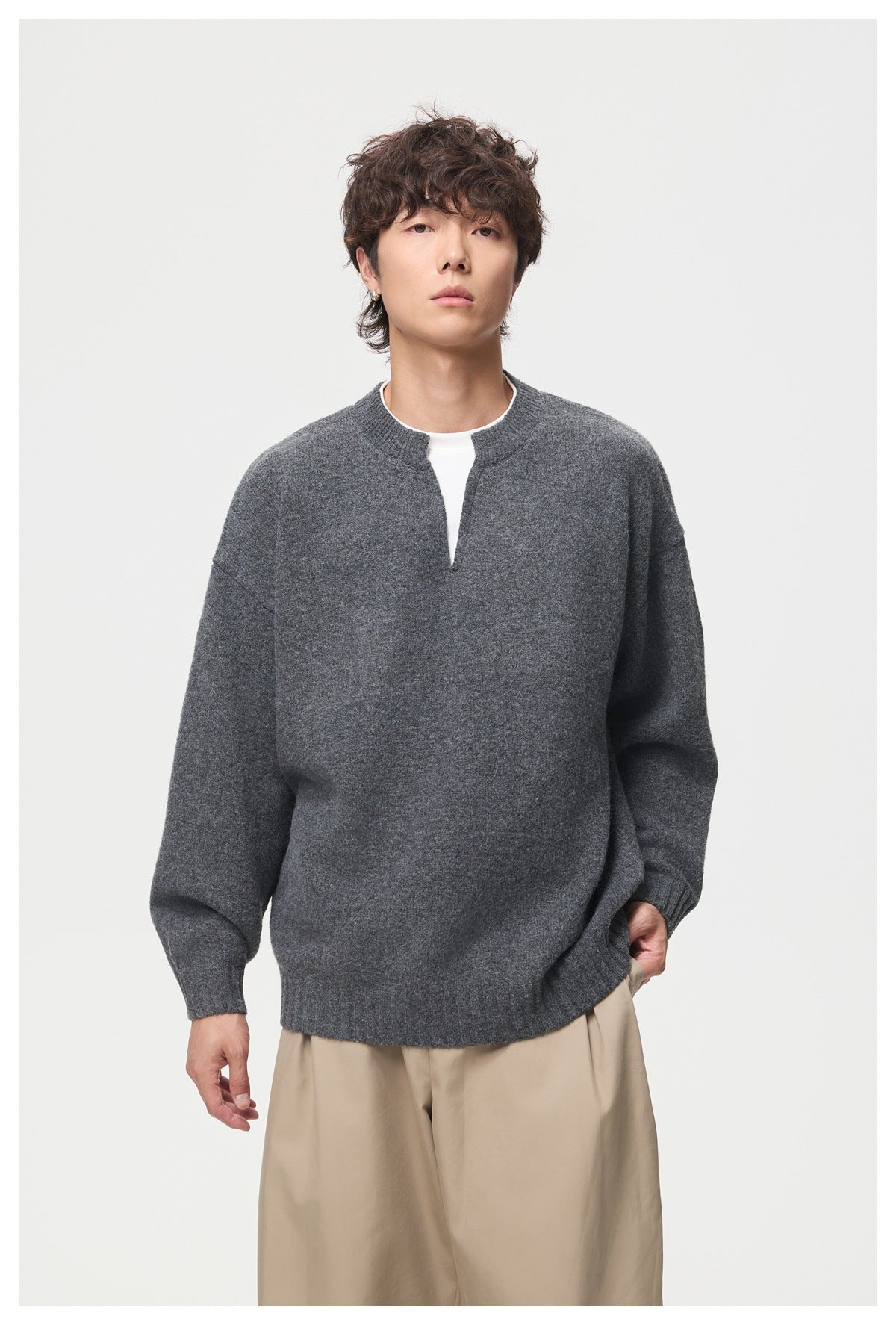 Front view of a model wearing a loose charcoal gray split-neck sweater over a white shirt.