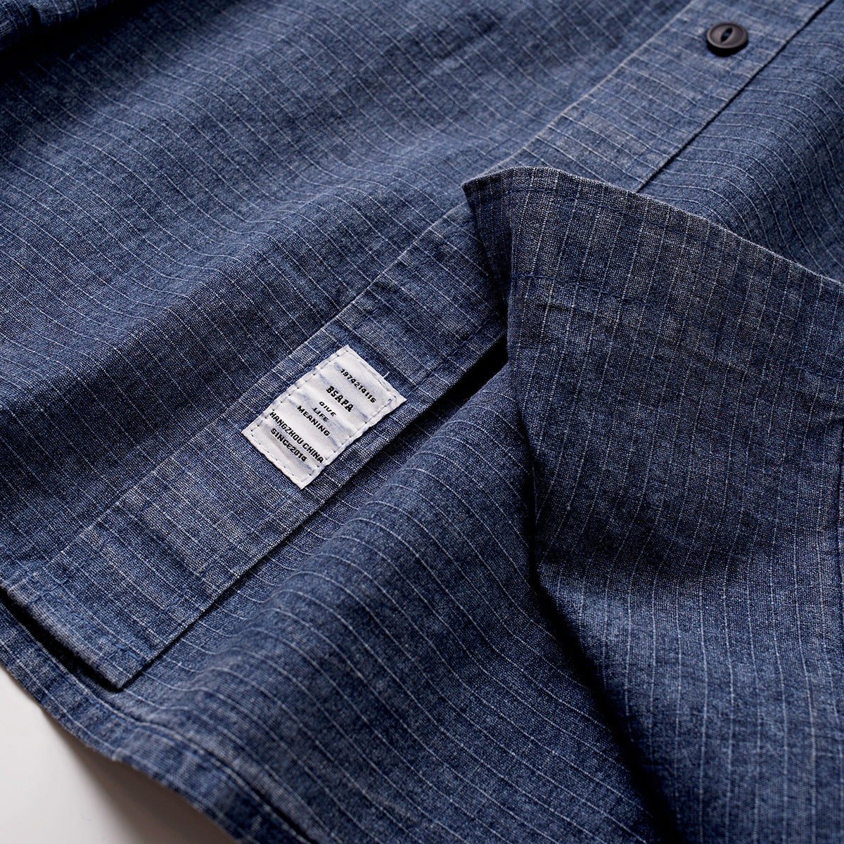 Close-up of a blue grid-patterned shirt showing its collar, button, and sewn-in label.