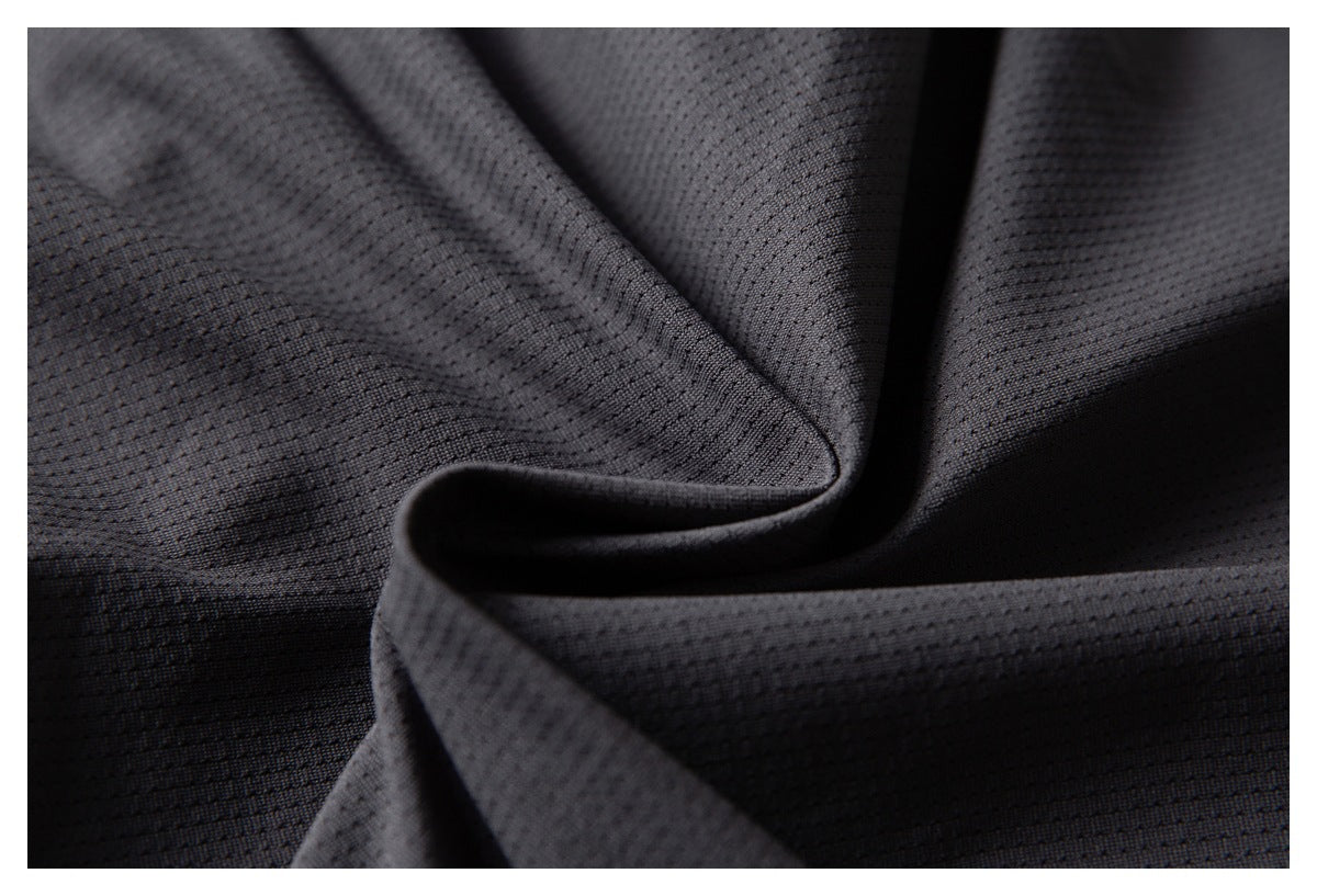 Close-up of dark charcoal fabric with a small perforated texture, draped in soft folds.