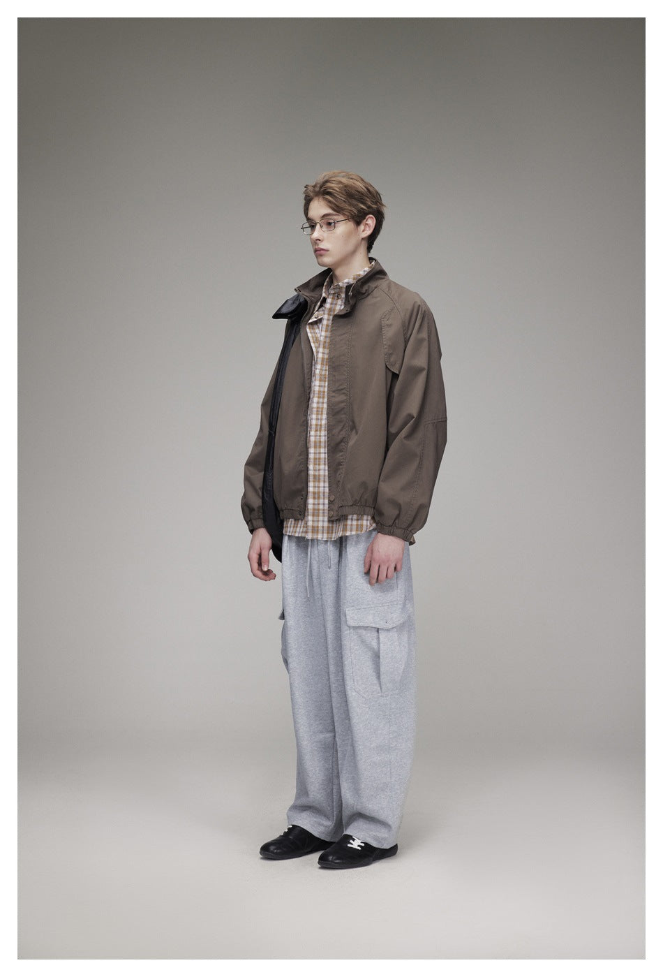 Full-length model in a brown zip-front jacket, checked shirt, gray cargo pants, and black shoes.
