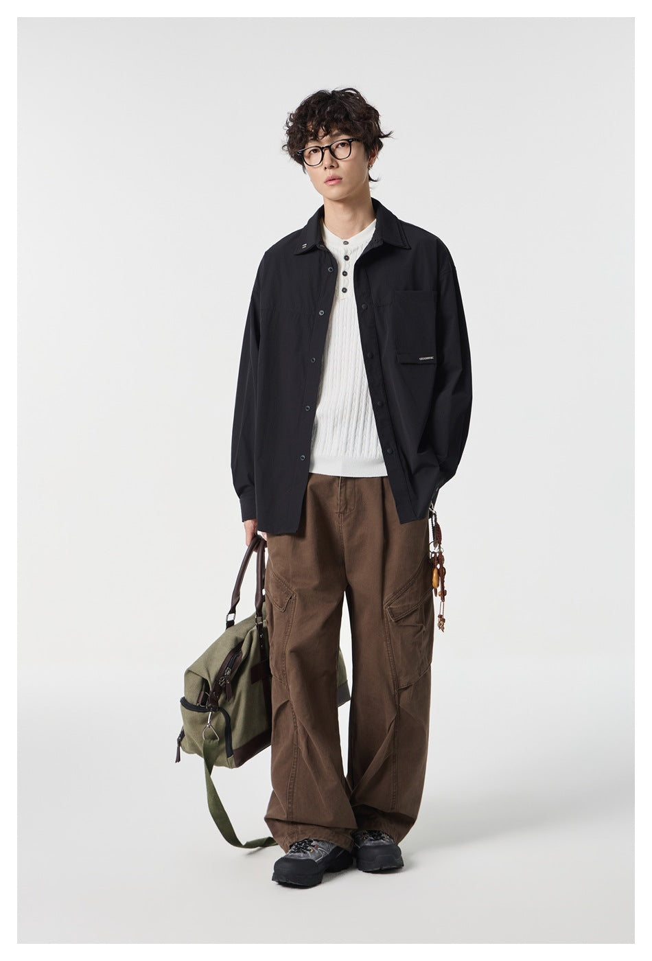 Full-length model wearing a black oversized button-front shirt over a white knit top with brown cargo trousers.