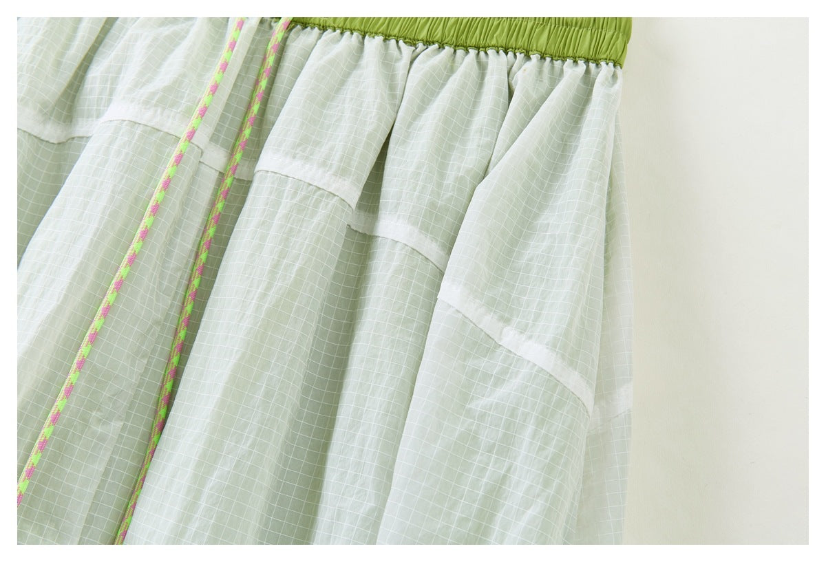 Close-up of the skirt's gathered pale green grid fabric, layered panels, and lime waistband with a multicolor drawcord.