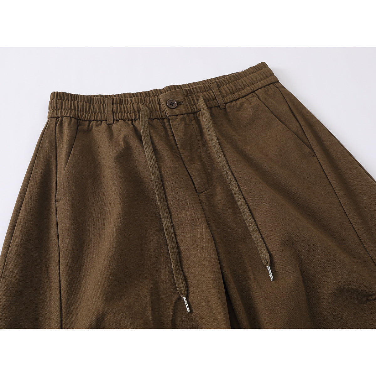 Close-up of brown wide-leg trousers showing an elasticated waistband, button, drawstrings, and front pleats.