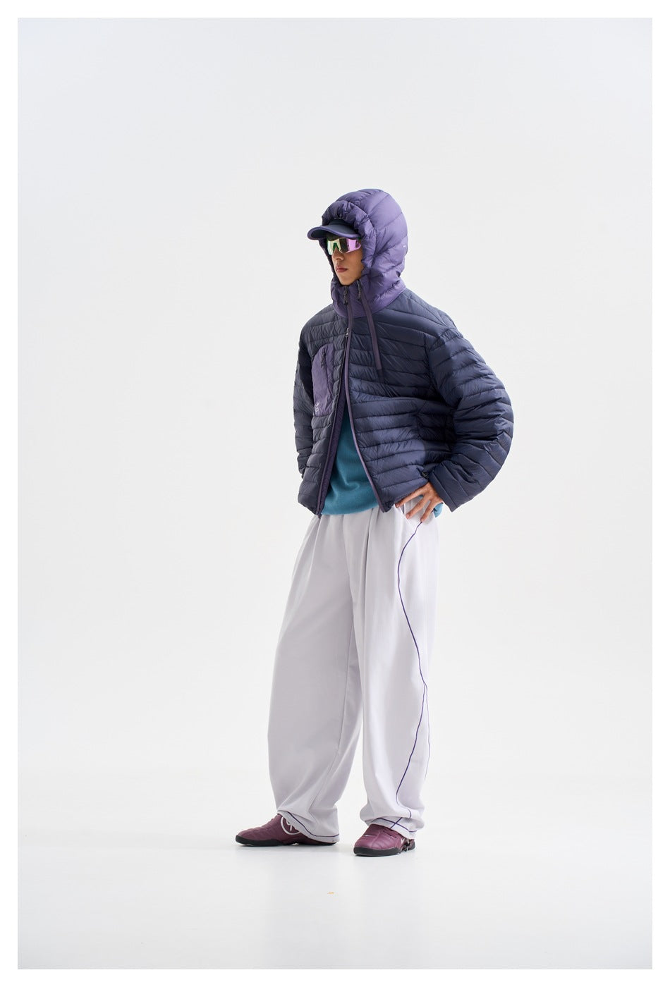 Full-length view of a person wearing a navy quilted jacket with a purple hood, white trousers and purple shoes.