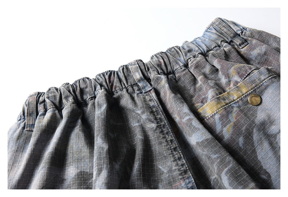 Close-up of gray plaid shorts showing the gathered elastic waistband, stitching, and a metal button.