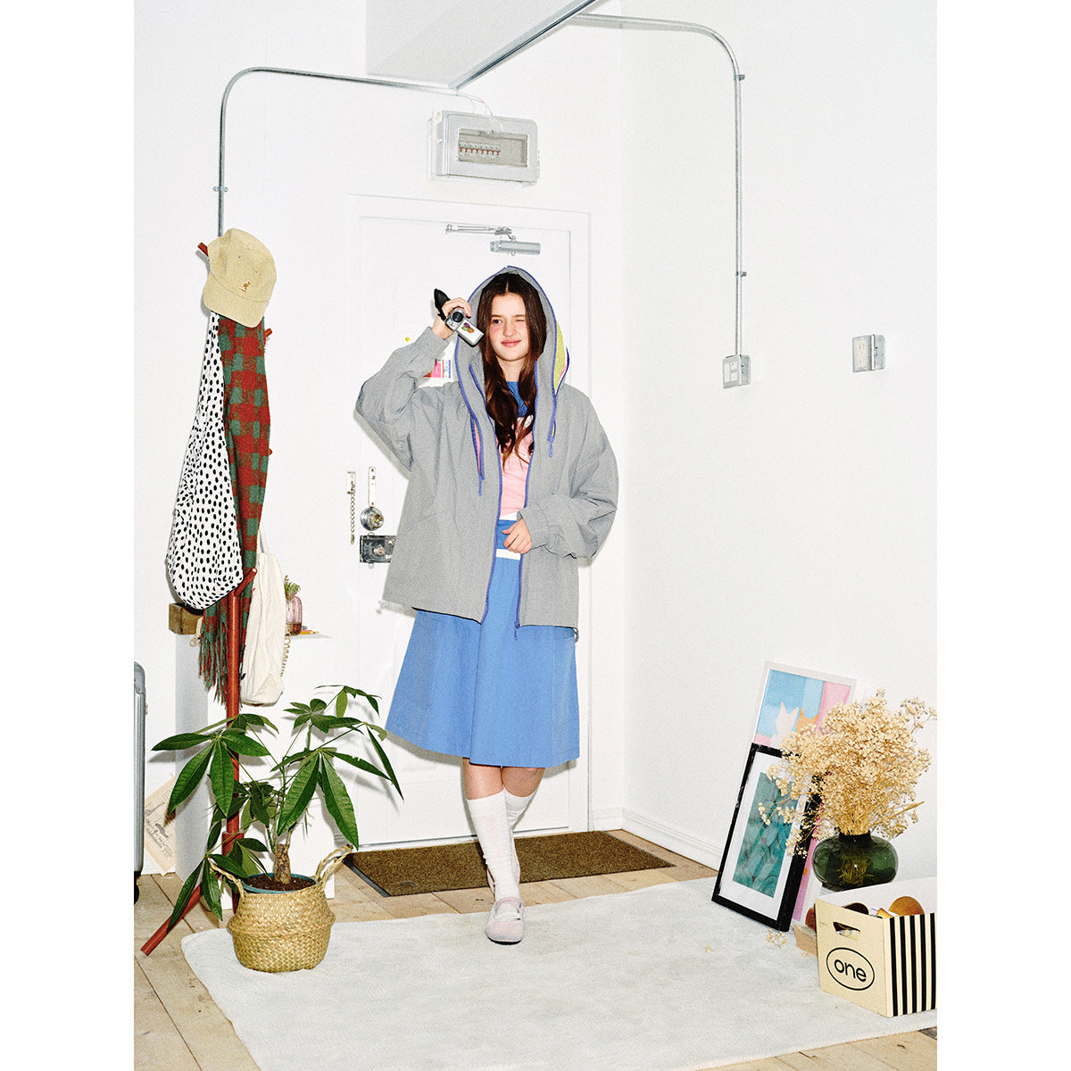 Model wears an open gray hooded jacket with blue trim and vivid lining over a blue dress.