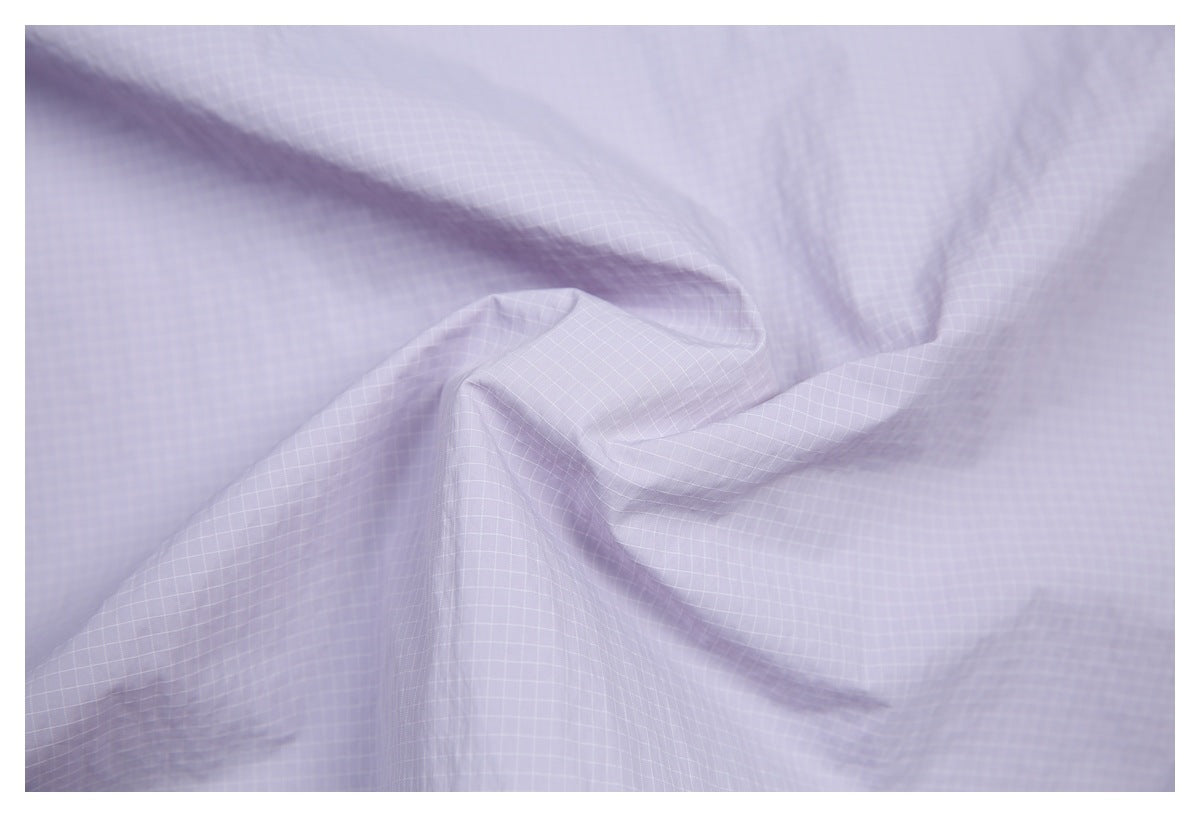 Close-up of pale lavender fabric with a fine white grid pattern and soft folds.