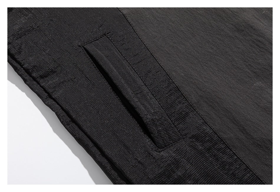 Close-up of a dark charcoal garment showing a narrow flap pocket and textured paneling.