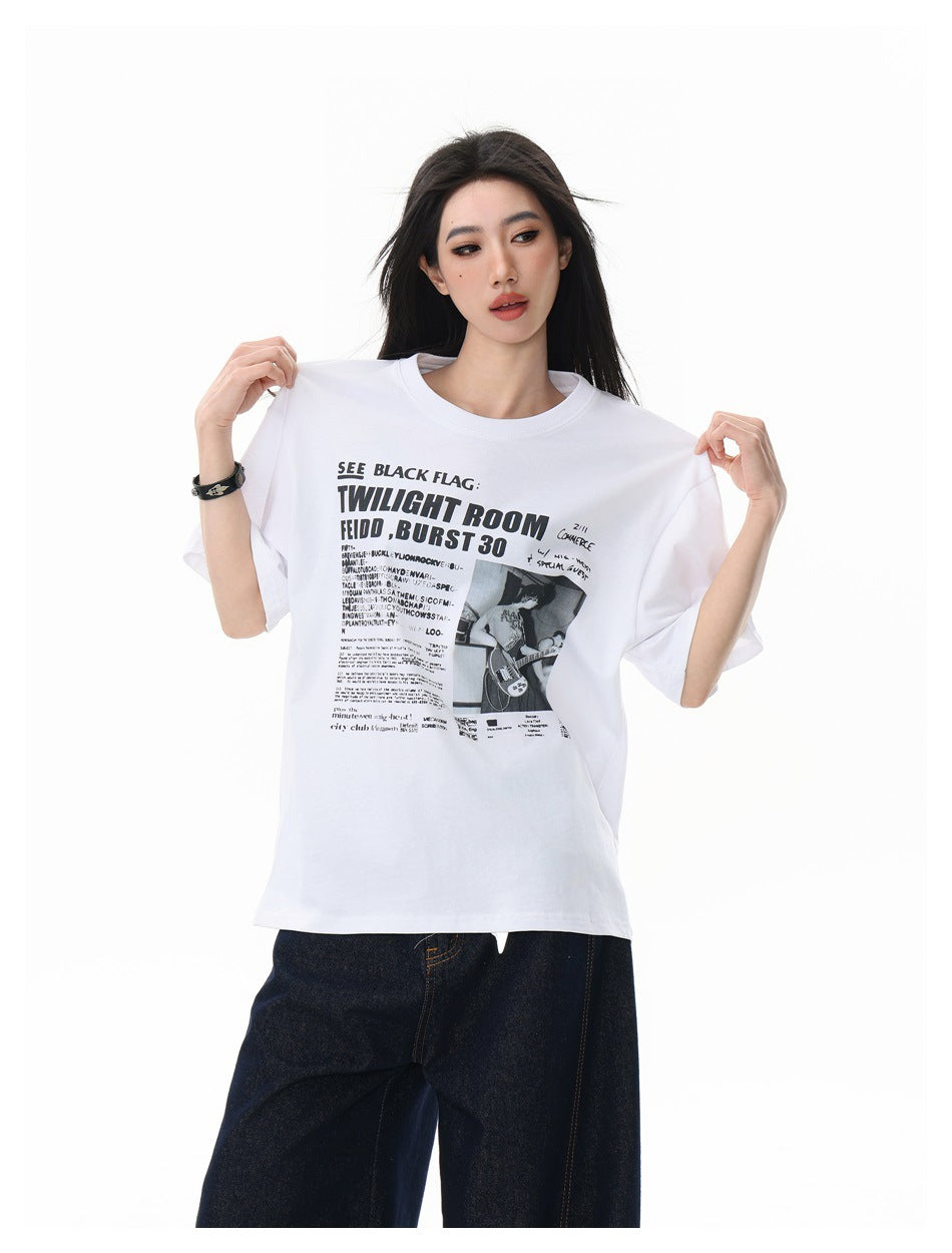 Model in the white oversized graphic T-shirt holding up the shoulders, with dark jeans, shown from the front